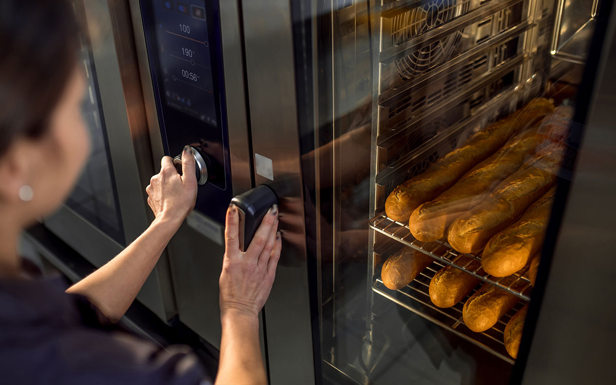 Frau schließt einen Backofen, der mit Baguettes gefüllt ist