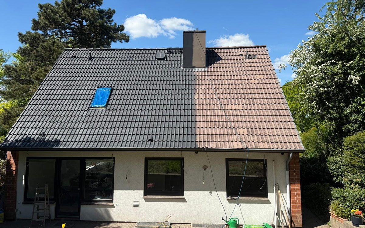 Zweifamilienhaus mit Schrägdach, das zur Hälfte gereinigt wurde. Die linke Dachhälfte erscheint dunkelgrau und sauber, während die rechte Seite noch mit hellen Verfärbungen und Schmutz bedeckt ist. Das Bild zeigt deutlich den Unterschied vor und nach der Dachreinigung.