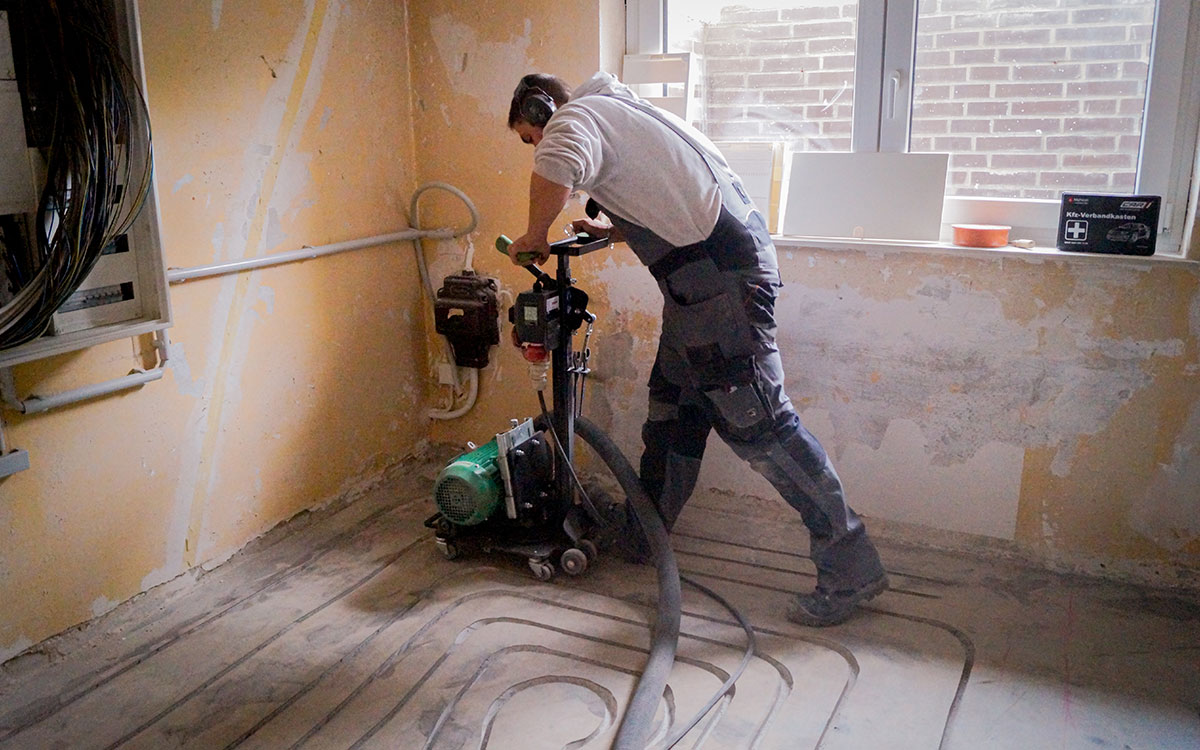 Ein Handwerker fräst präzise Leitungsrillen in den Boden für eine neue Fußbodenheizung.